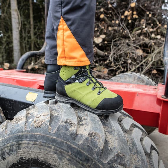 Pilčík v topánkach HAIX Protector Ultra 2.0 GTX stojaci na pneumatike lesného stroja.