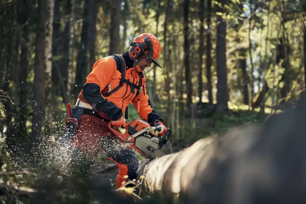 Profesionálny pilčík v akcii s motorovou pílou, oblečený v bunde Husqvarna Technical Extreme v reálnom lesnom prostredí.