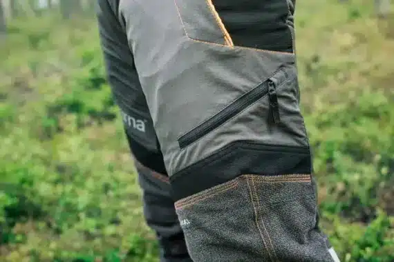 Protiporezové nohavice: Detail bočného vrecka na zips na sivých protiporezových nohaviciach Husqvarna Technical v lese.