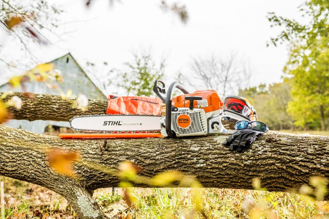 Motorová píla STIHL MS 362 s ochrannou výbavou (prilba, rukavice) leží na spílenom kmeni stromu.