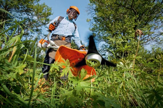 Muž v ochrannej výbave pracuje s krovinorezom STIHL FS 240 C-E v hustej tráve.