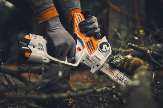 Osoba v rukaviciach používa akumulátorovú pílu STIHL GTA 40 na rezanie konárov v záhrade.